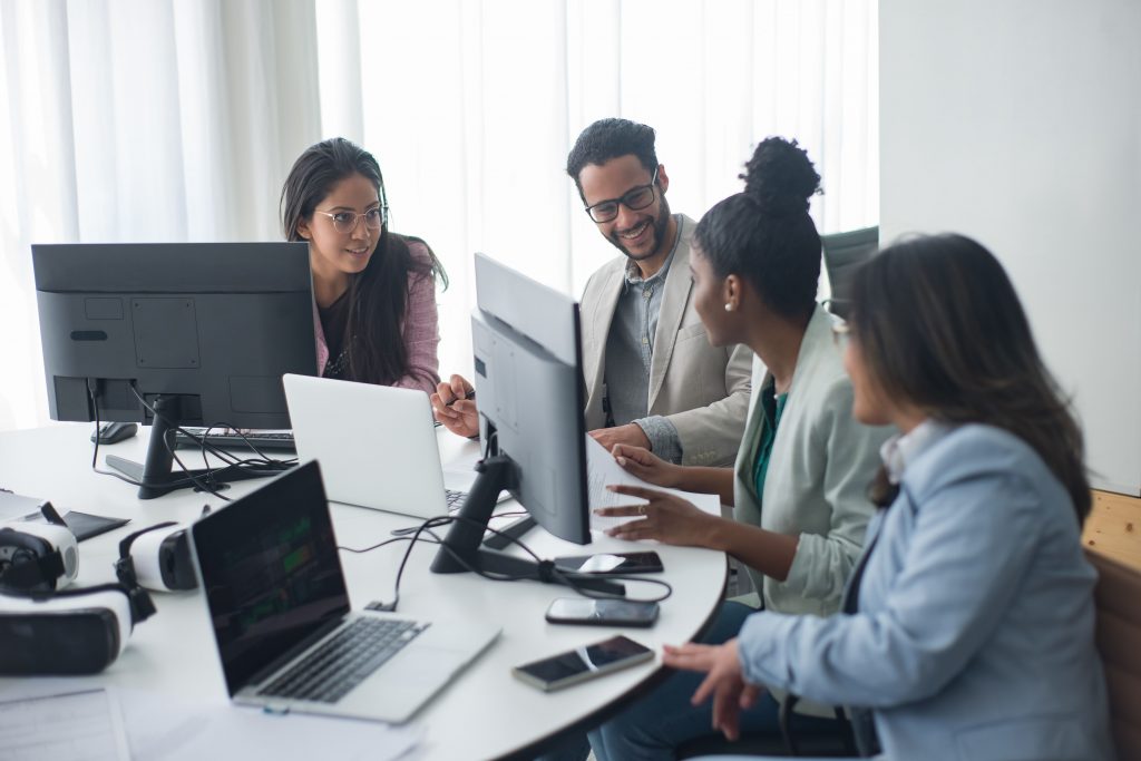 A diverse team engages in discussion around computers in a modern office setting.
